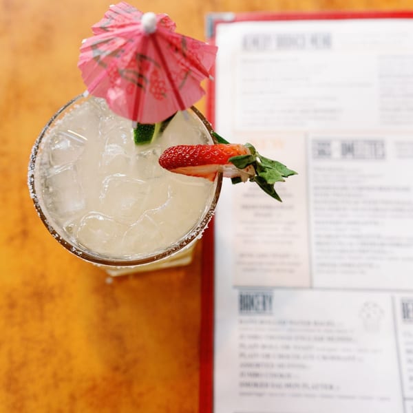 Overhead view of a Remedy Diner margarita with a strawberry, lime, and pink umbrella.