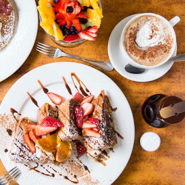 Remedy Diner's French toast with strawberries, chocolate drizzle, fruit cup, and cappuccino.