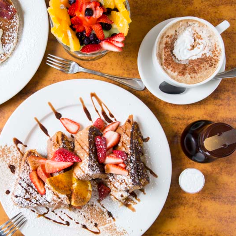 Remedy Diner's French toast with strawberries, chocolate drizzle, fruit cup, and cappuccino.