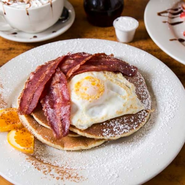 Remedy Diner's pancakes with bacon, a fried egg, orange slices, and powdered sugar.