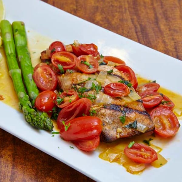 Grilled fish with cherry tomatoes, onions, and asparagus on a white rectangular plate at Remedy Diner.