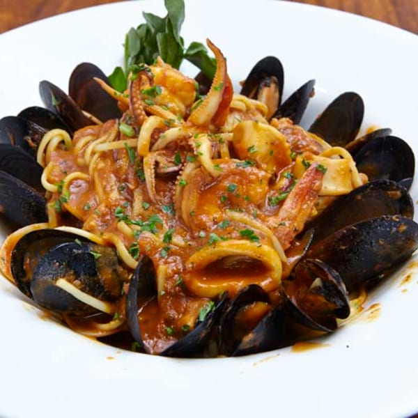 Seafood pasta with mussels, squid, and octopus in a rich red sauce, garnished with parsley.