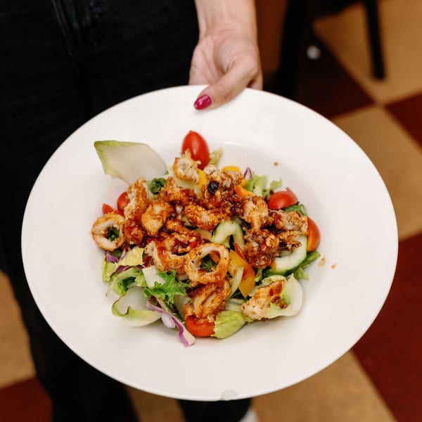 A Remedy Diner salad with fried calamari, mixed greens, tomatoes, and cucumbers on a white plate.