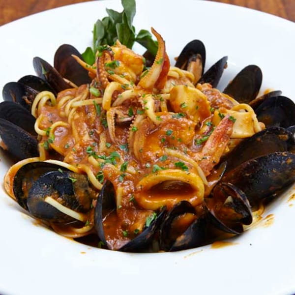 A white bowl of Remedy Diner's seafood pasta with mussels, calamari, and a rich red sauce.