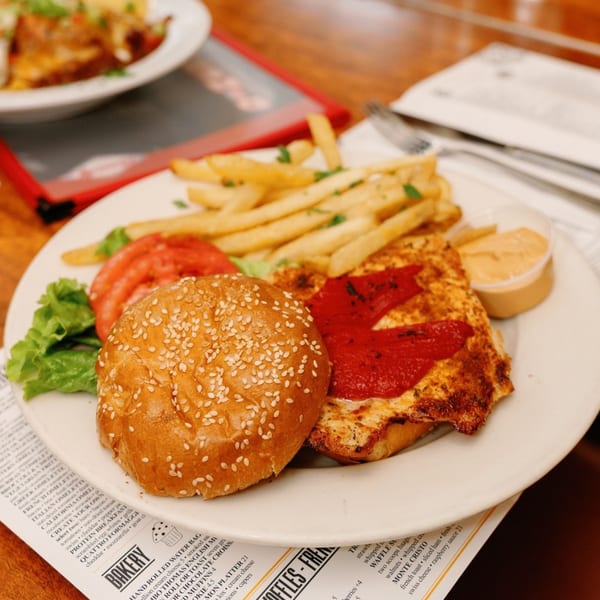 A Remedy Diner plate with a chicken sandwich, fries, lettuce, tomatoes, and dipping sauce.