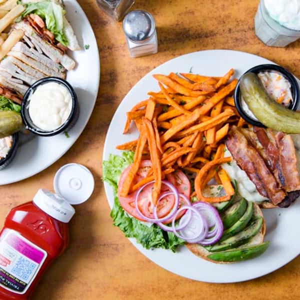A Remedy Diner burger with bacon, avocado, and sweet potato fries, alongside a club sandwich.