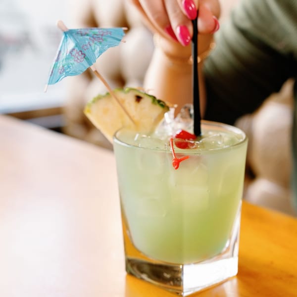 A Remedy Diner cocktail with a pineapple slice, cherries, and a blue umbrella.