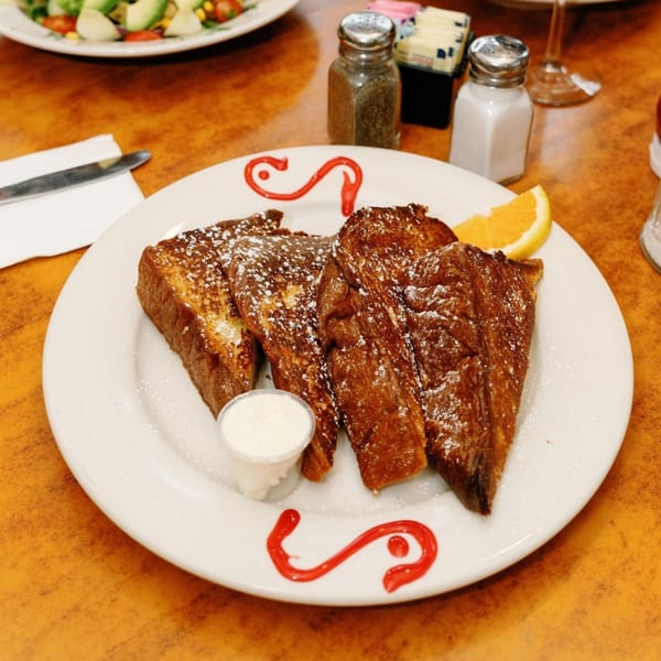 Remedy Diner's French toast, dusted with powdered sugar, served with whipped cream and an orange slice.