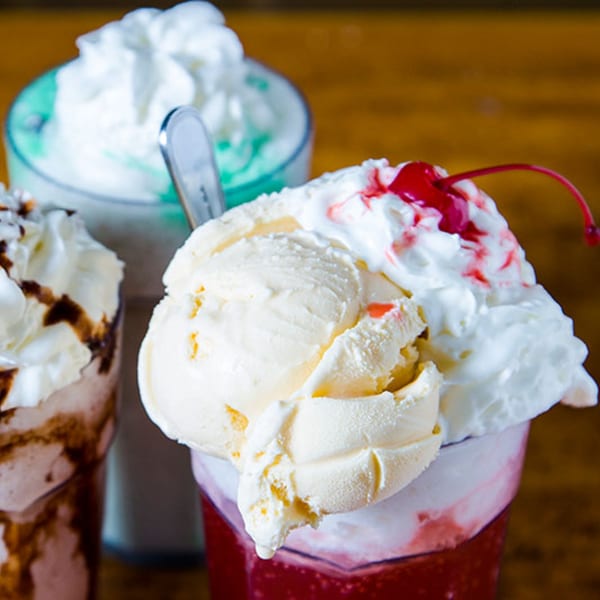 Three diner milkshakes, one vanilla with a cherry, one chocolate, and one mint, topped with whipped cream.