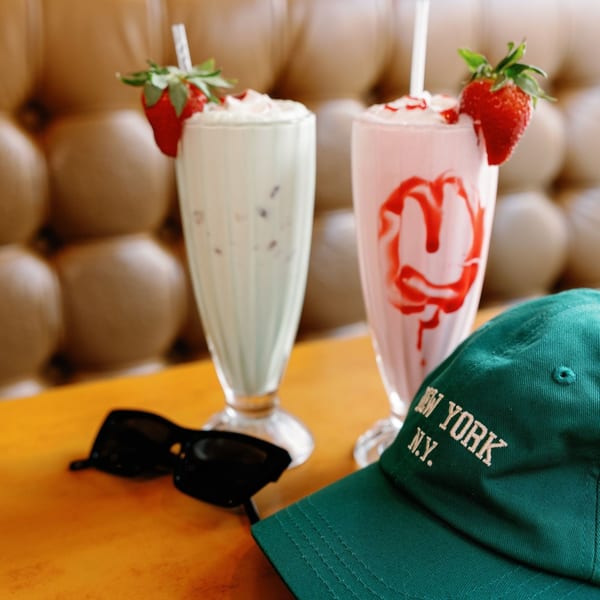 Two Remedy Diner milkshakes, one green and one pink with strawberry, on a table with sunglasses and a hat.