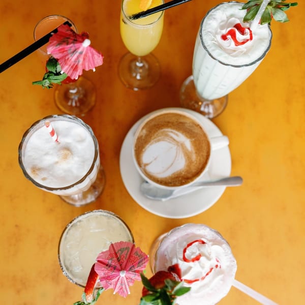 Overhead view of various diner drinks, including coffee, milkshakes, and cocktails, on a yellow table.